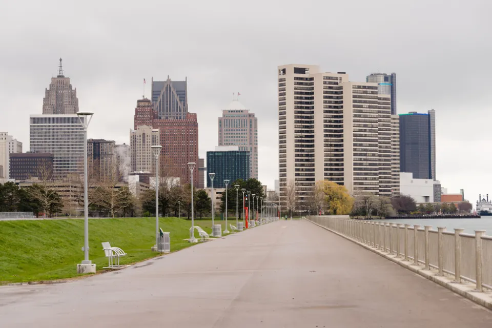 Waterfront walkway with benches and Detroit skyline in the background